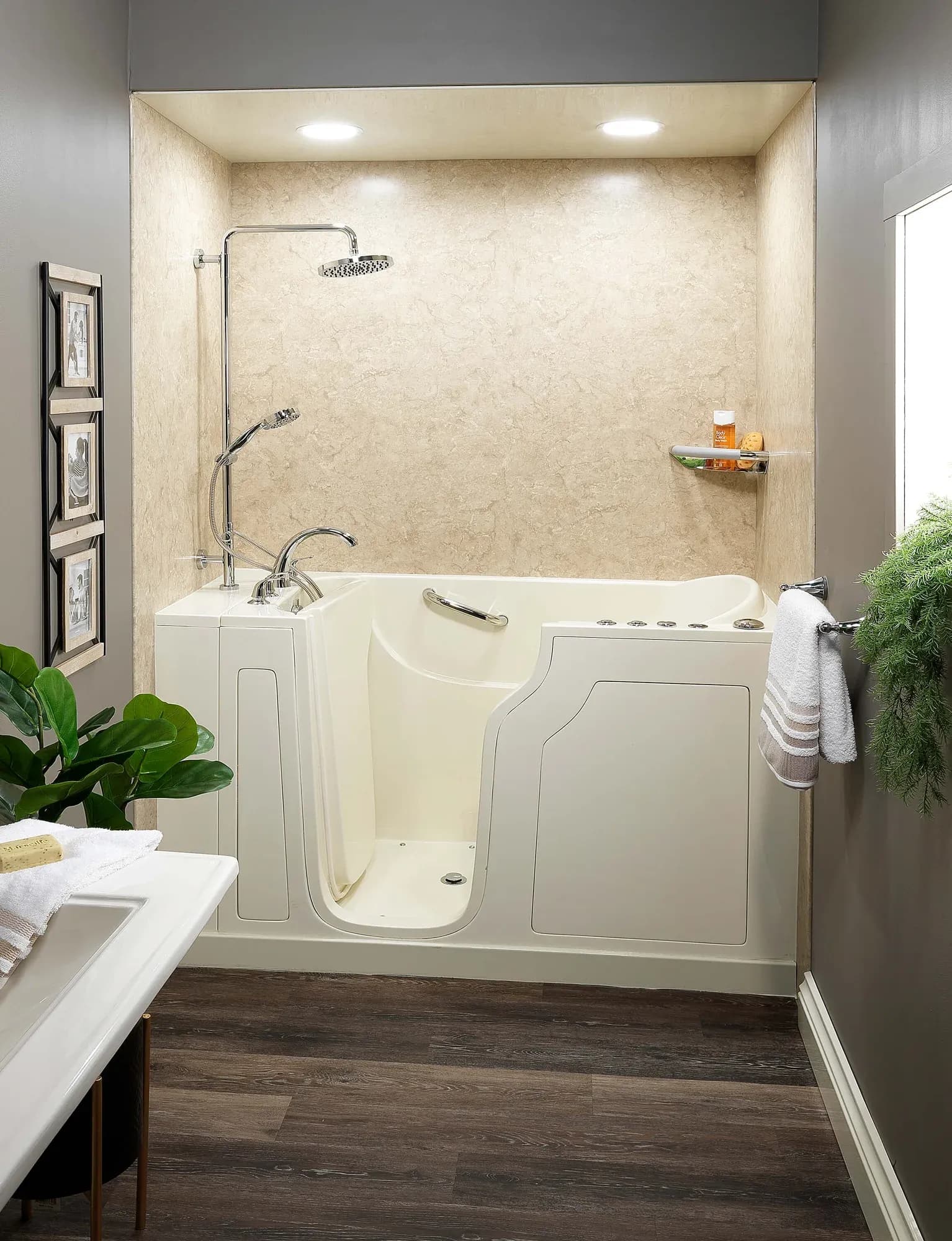 Accessible bathroom with beige walk-in tub, overhead shower, and decorative plants. Modern and functional design with warm-toned flooring and soft lighting.